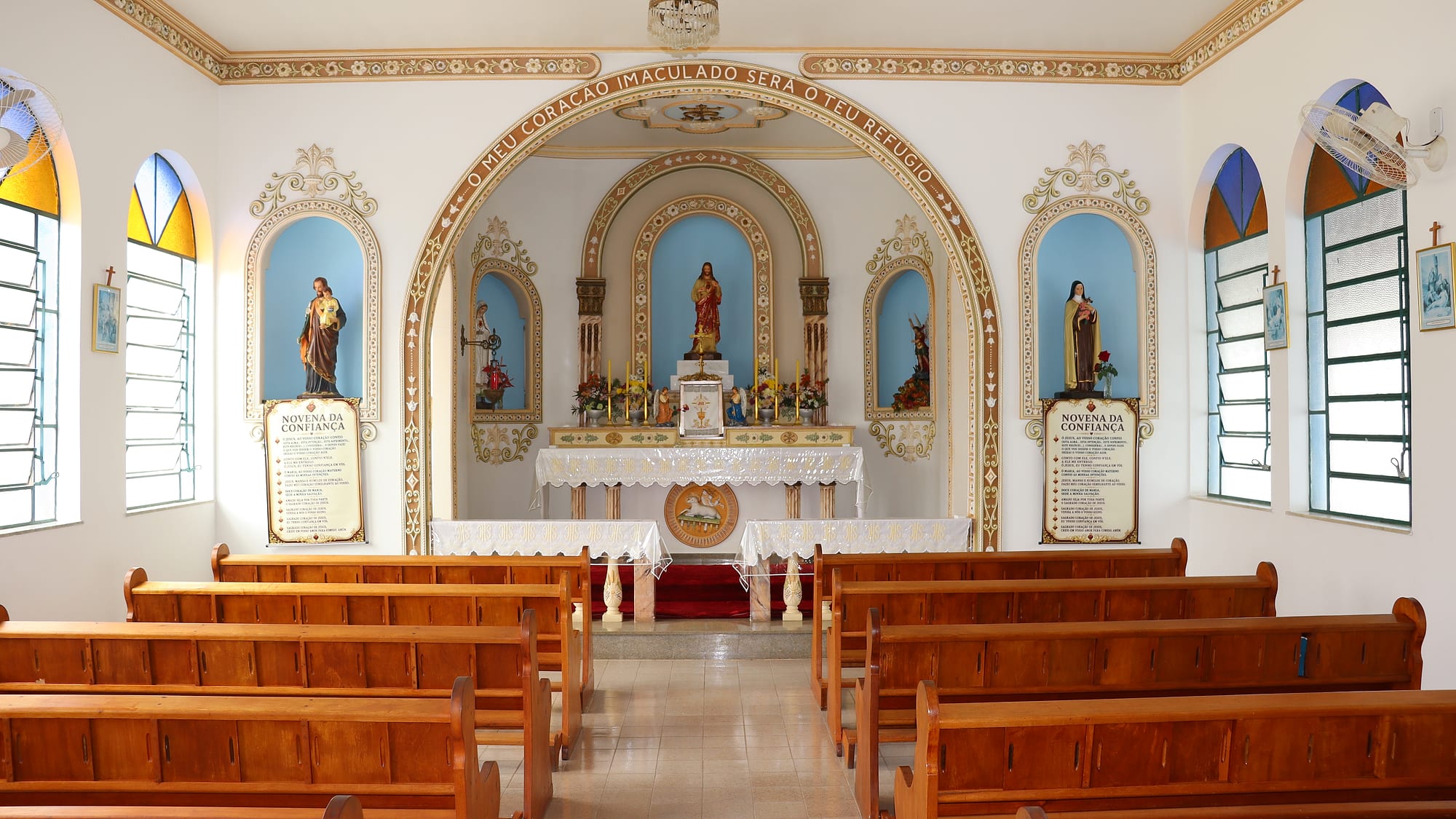 Interior da capela do Colégio, com o altar, as imagens nos nichos e os bancos de madeira