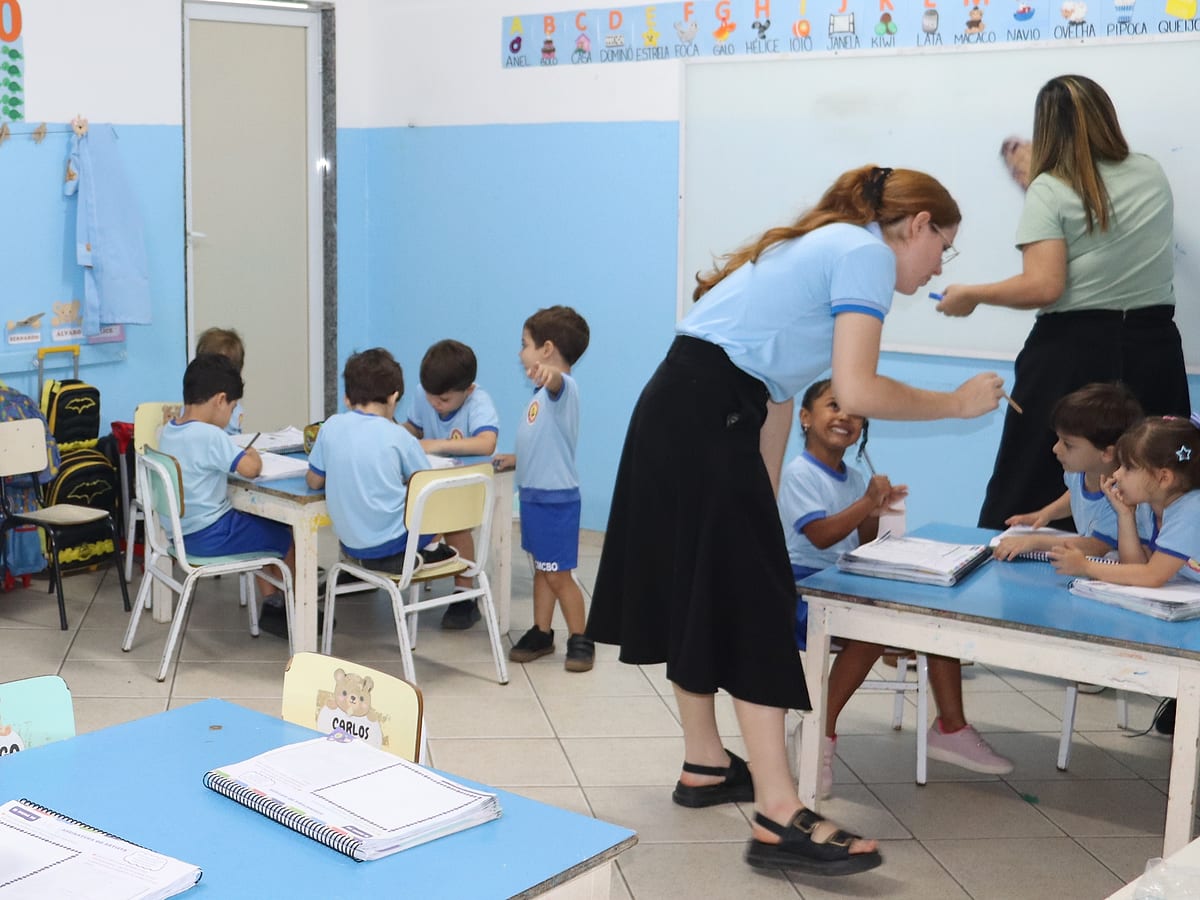 Professora ajudando as crianças da Educação Infantil nas atividades da mesa