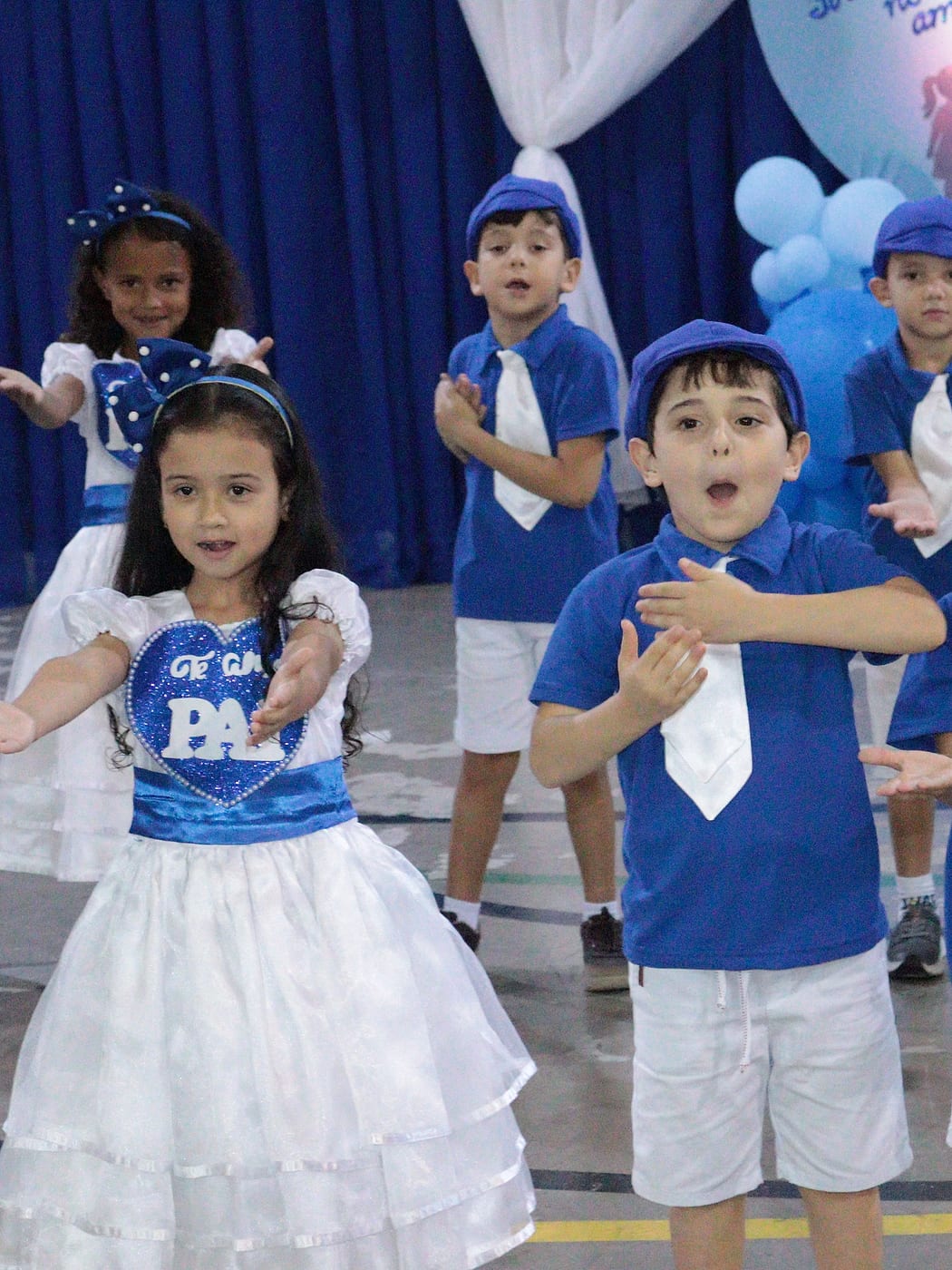 Crianças da Educação Infantil de boné azul dançando numa apresentação