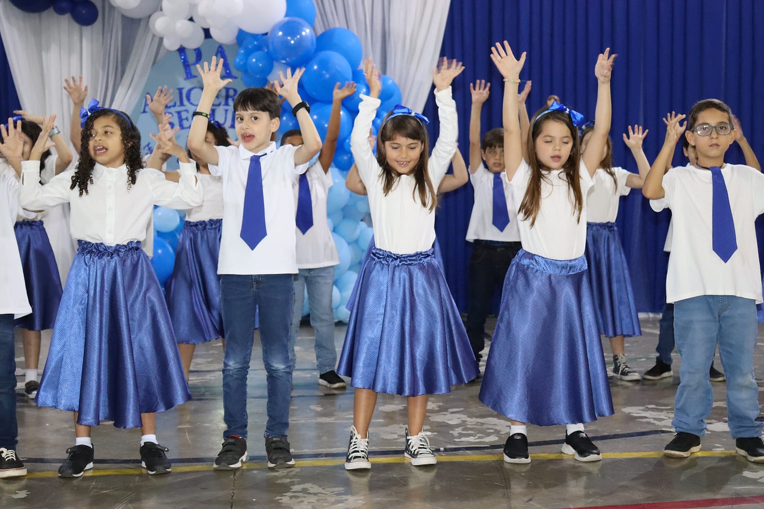Alunos do Fundamental I de braços para cima numa apresentação