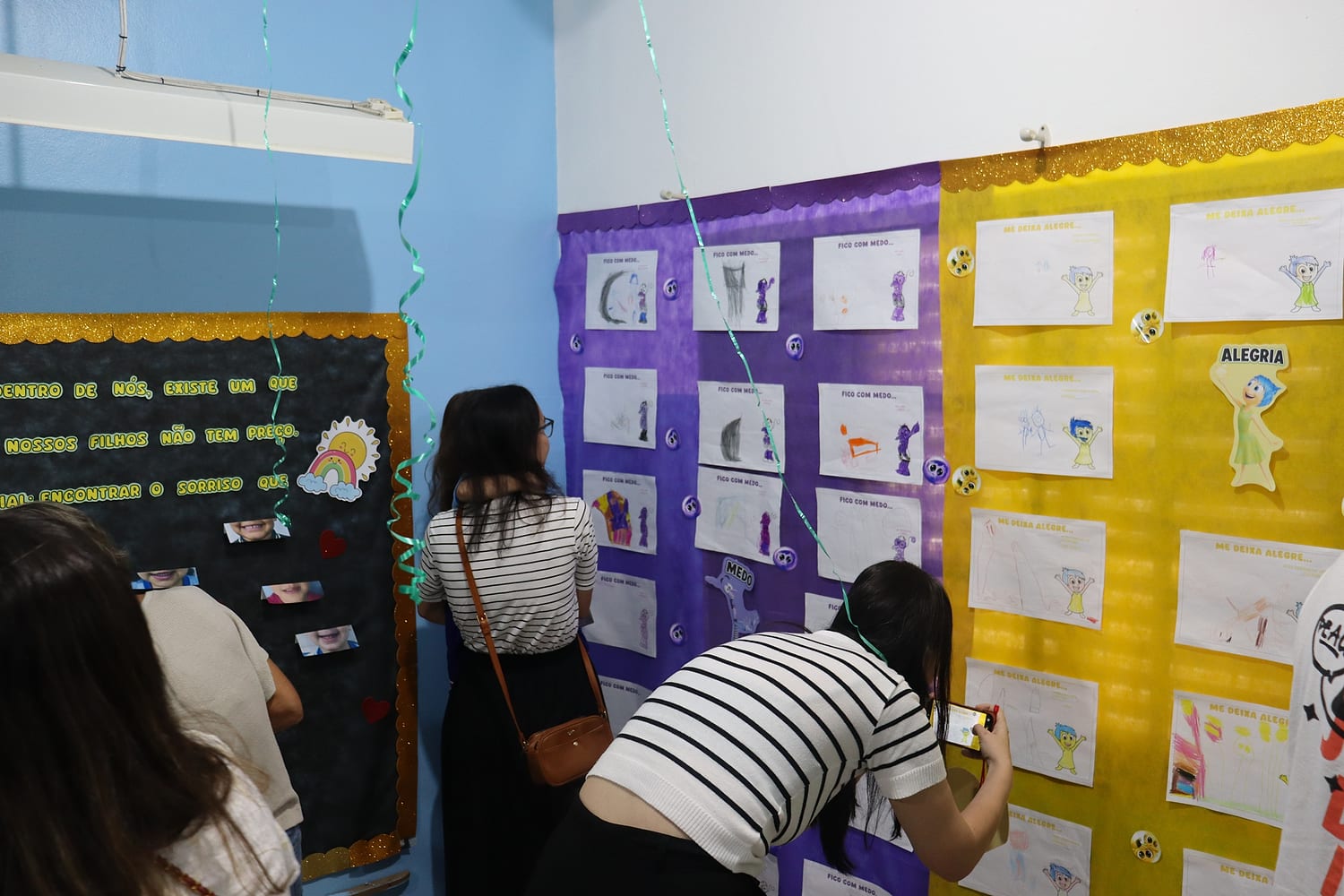 Famílias olhando os trabalhos das crianças expostos no mural
