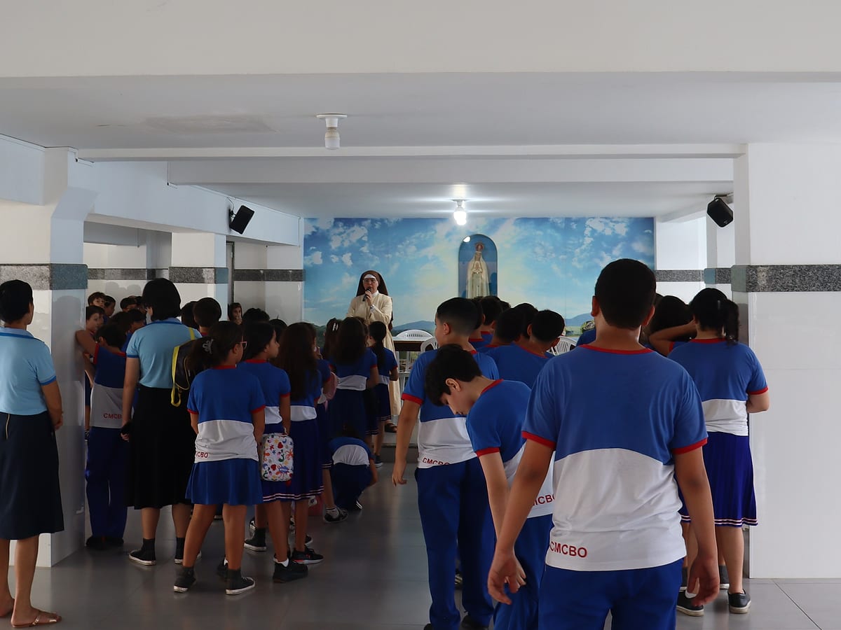 Alunos reunidos no pátio, de costas, diante da imagem de Nossa Senhora, na acolhida da manhã