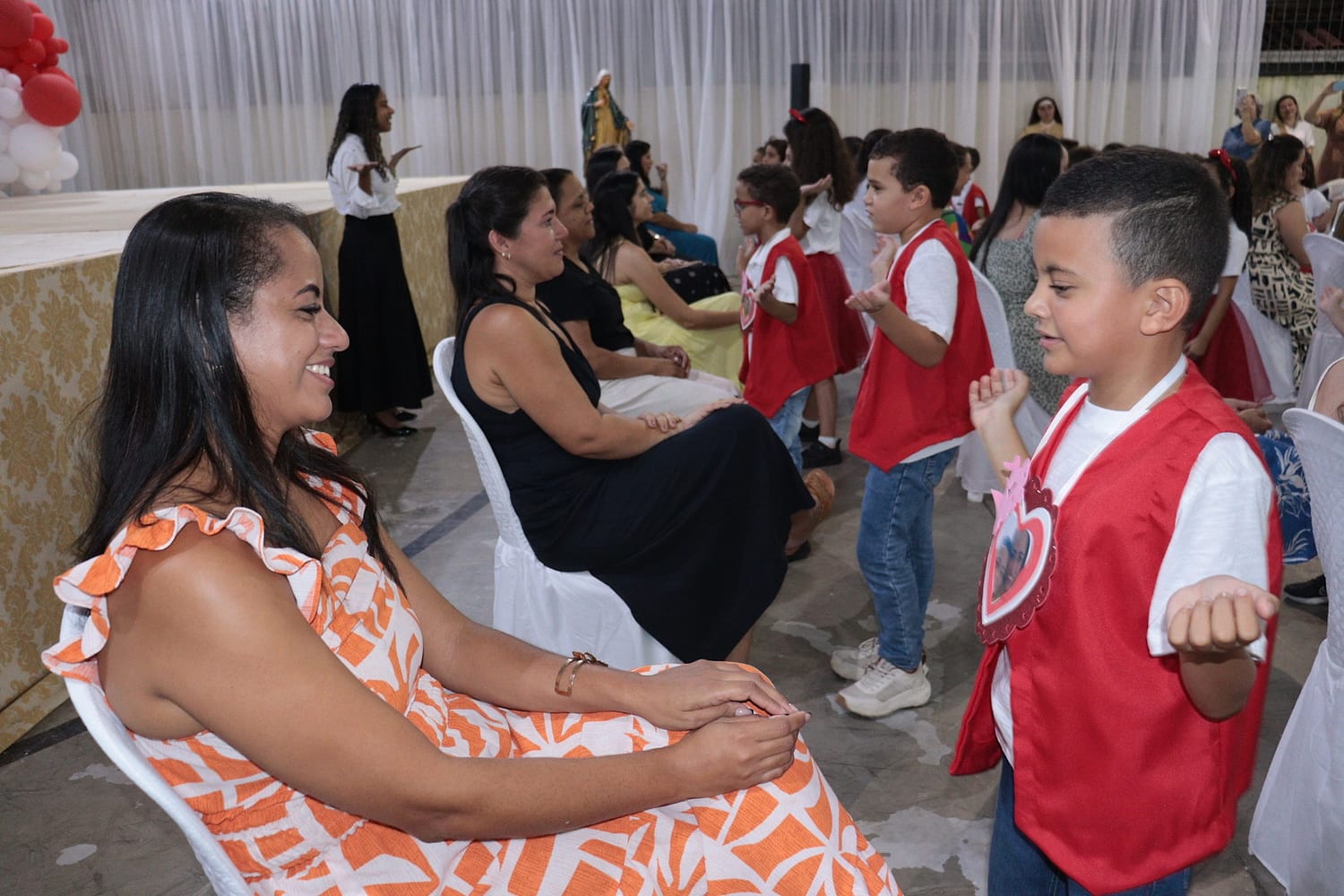 Menino de colete vermelho dançando diante da mãe
