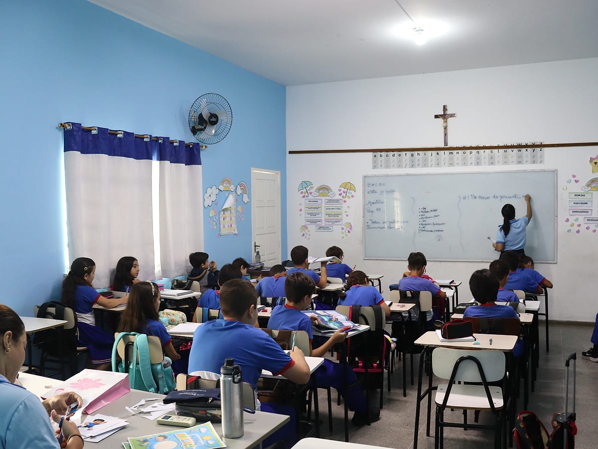 Professora escrevendo no quadro e a turma de uniforme nas carteiras